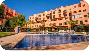 Ein Hotel mit Swimmingpool, mehreren Balkonen und Palmen.
