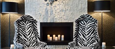 Ein stilvoller Lounge-Bereich mit zwei Sesseln in Zebra-Optik, die einen Kamin mit brennenden Kerzen gegenüberhaben.