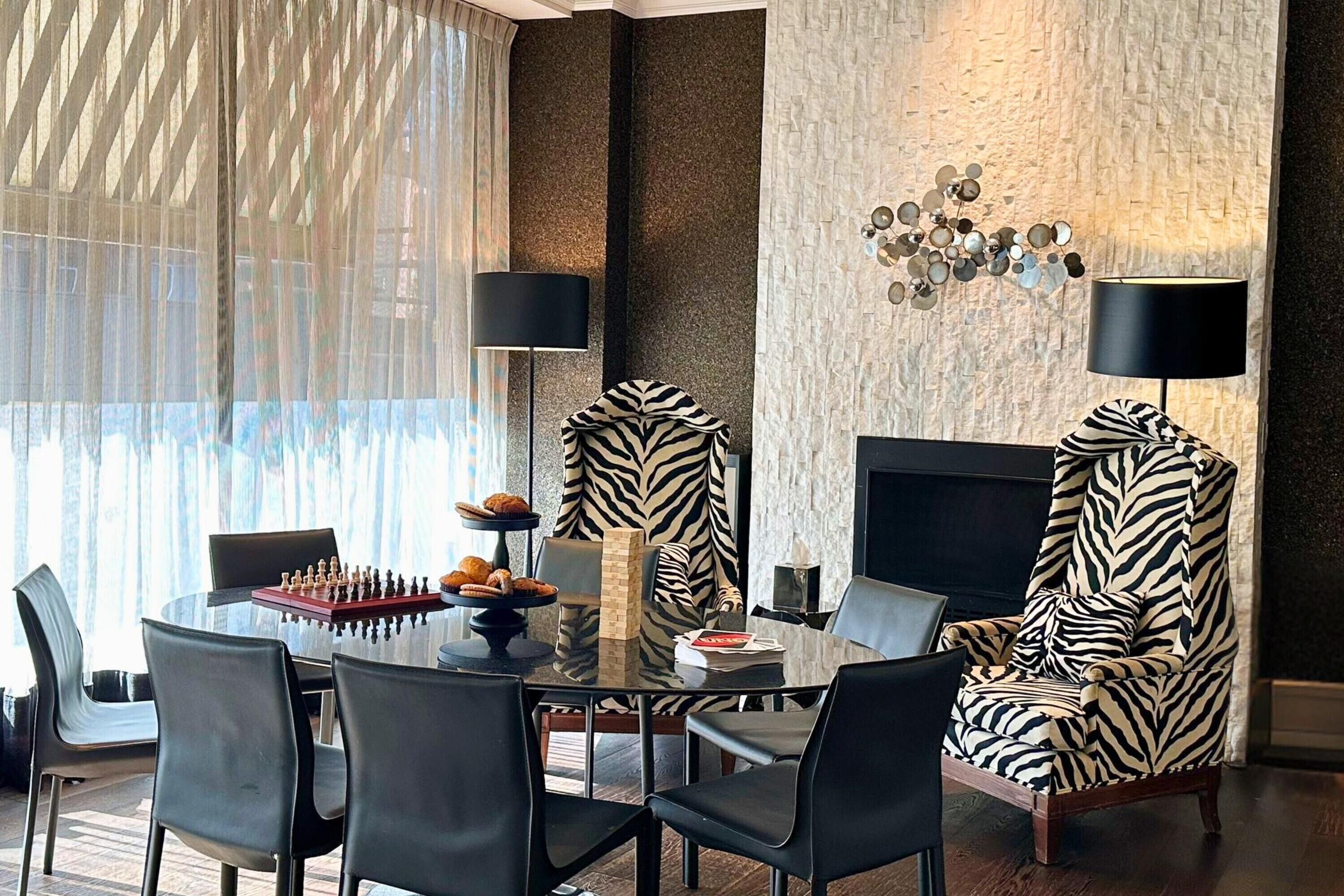 Un comedor moderno con una mesa de vidrio, sillas negras y un sillón estampado con diseño de cebra.