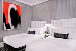 A hotel room with two beds, a modern abstract painting, and a small table with a lamp. - Moderne | Deluxe Double | Steps to Broadway | 24/7 Guest Lounge (New York)