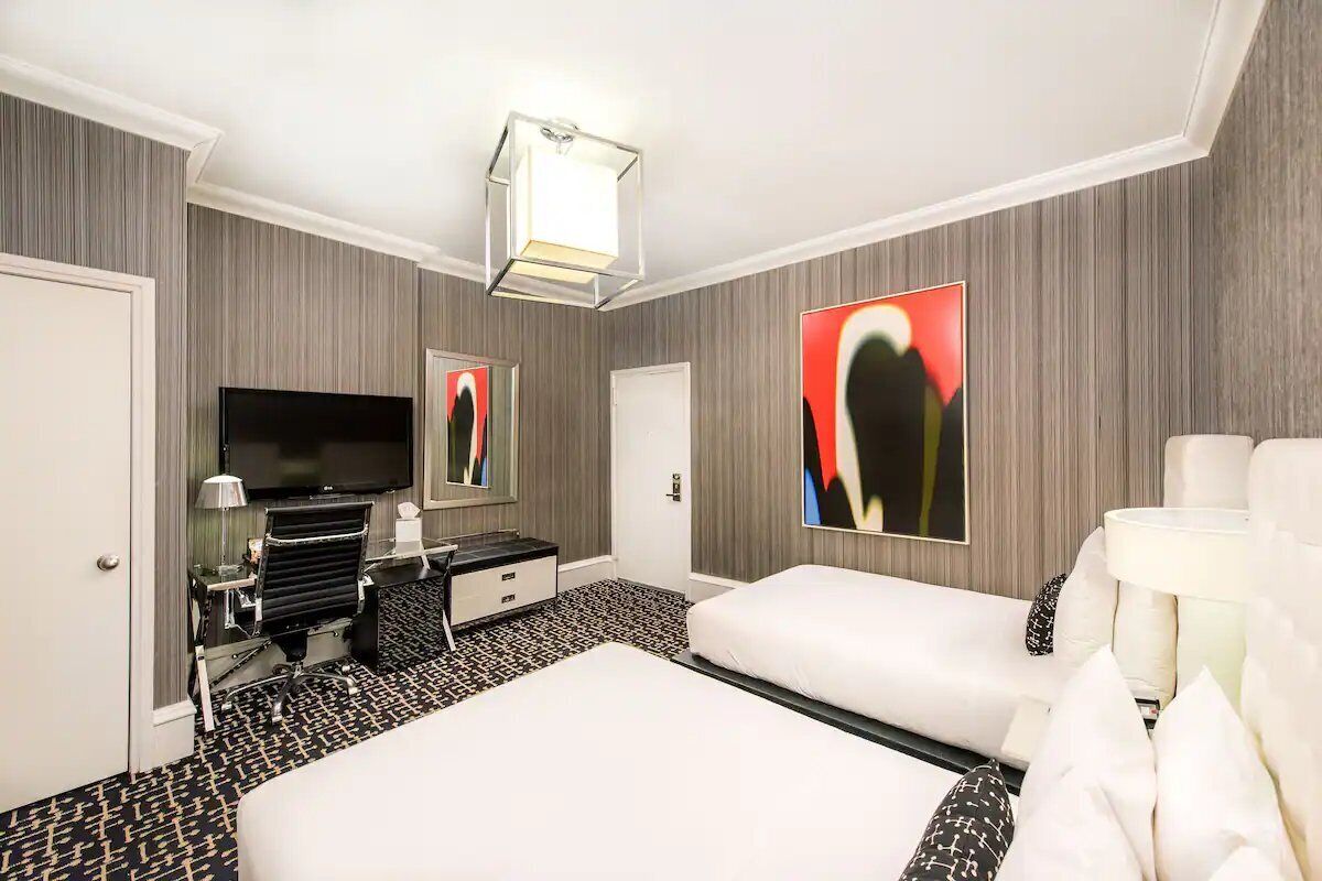 Habitación de hotel con una cama grande, un televisor de pantalla plana, un escritorio con lámpara y obras de arte en las paredes.