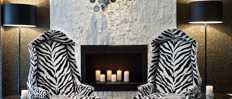 A modern lounge area with two zebra-patterned armchairs facing a fireplace with lit candles.