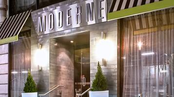 Entrada de hotel con un llamativo letrero 'MODERNE', fachada de vidrio y una escalera que conduce a la entrada.