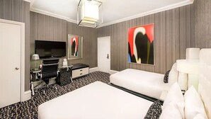 Ein Hotelzimmer mit einem großen Bett, einem Flachbildfernseher, einem Schreibtisch mit Lampe und Kunstwerken an den Wänden.