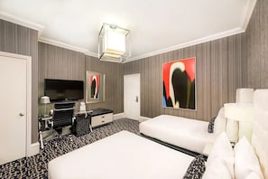 Ein Hotelzimmer mit einem großen Bett, einem Flachbildfernseher, einem Schreibtisch mit Lampe und Kunstwerken an den Wänden.