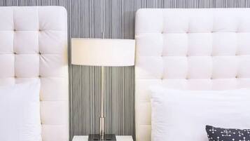 Una habitación con dos cabeceros blancos con capitoné, una lámpara de pie y un cojín estampado.