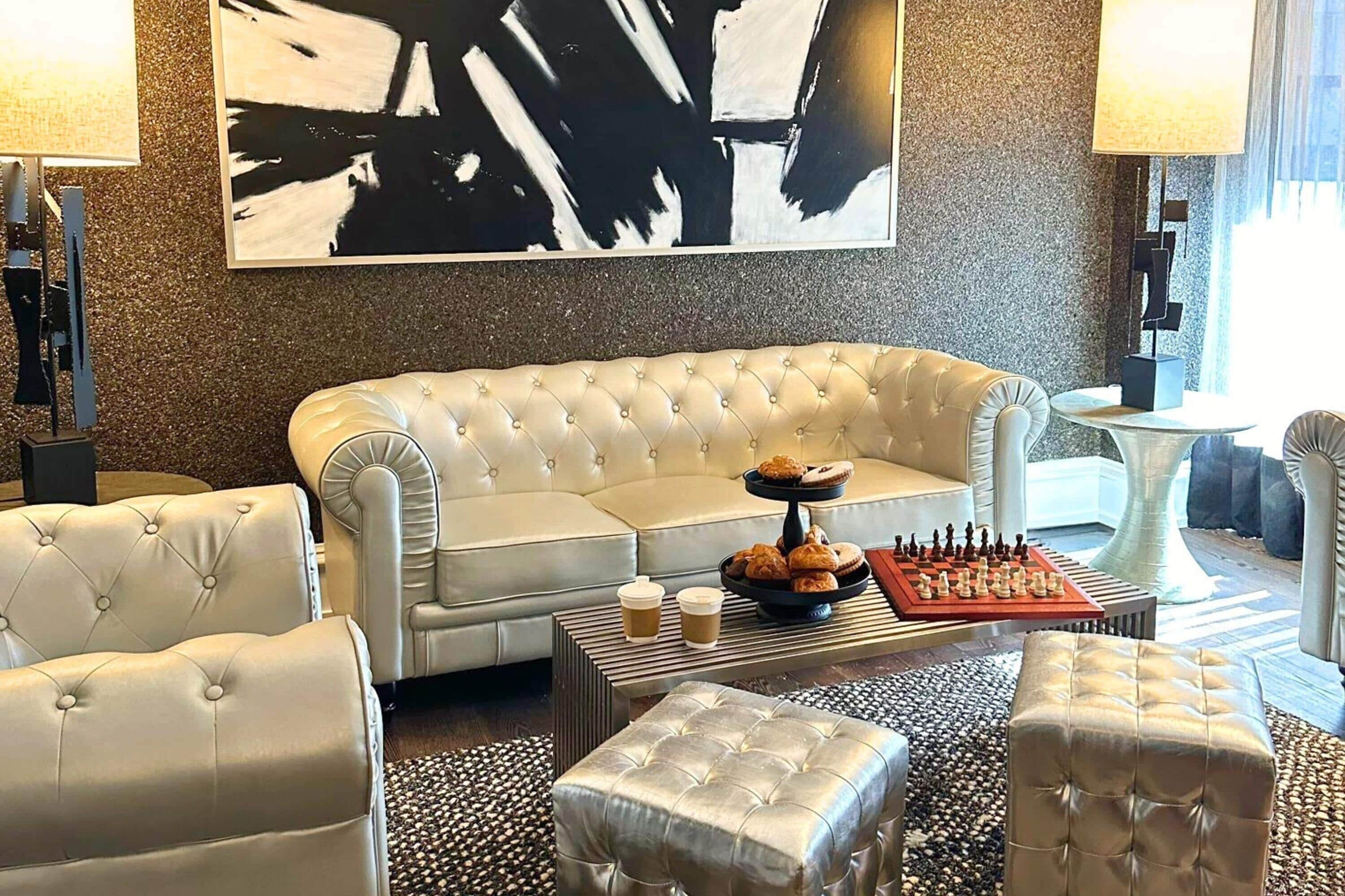 Una sala de estar moderna con un sofá capitonado, una mesa de centro con pasteles y un tablero de ajedrez.