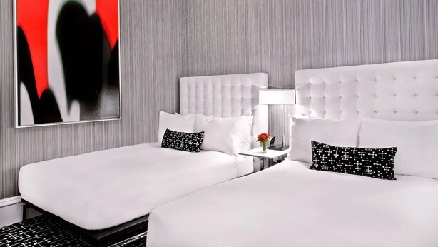 Et hotelværelse med to senge, et moderne abstrakt maleri og et lille bord med en lampe.