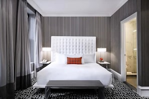 Ein Hotelzimmer mit einem großen Bett, einem Kopfteil, Nachttischen und einer Badezimmertür.