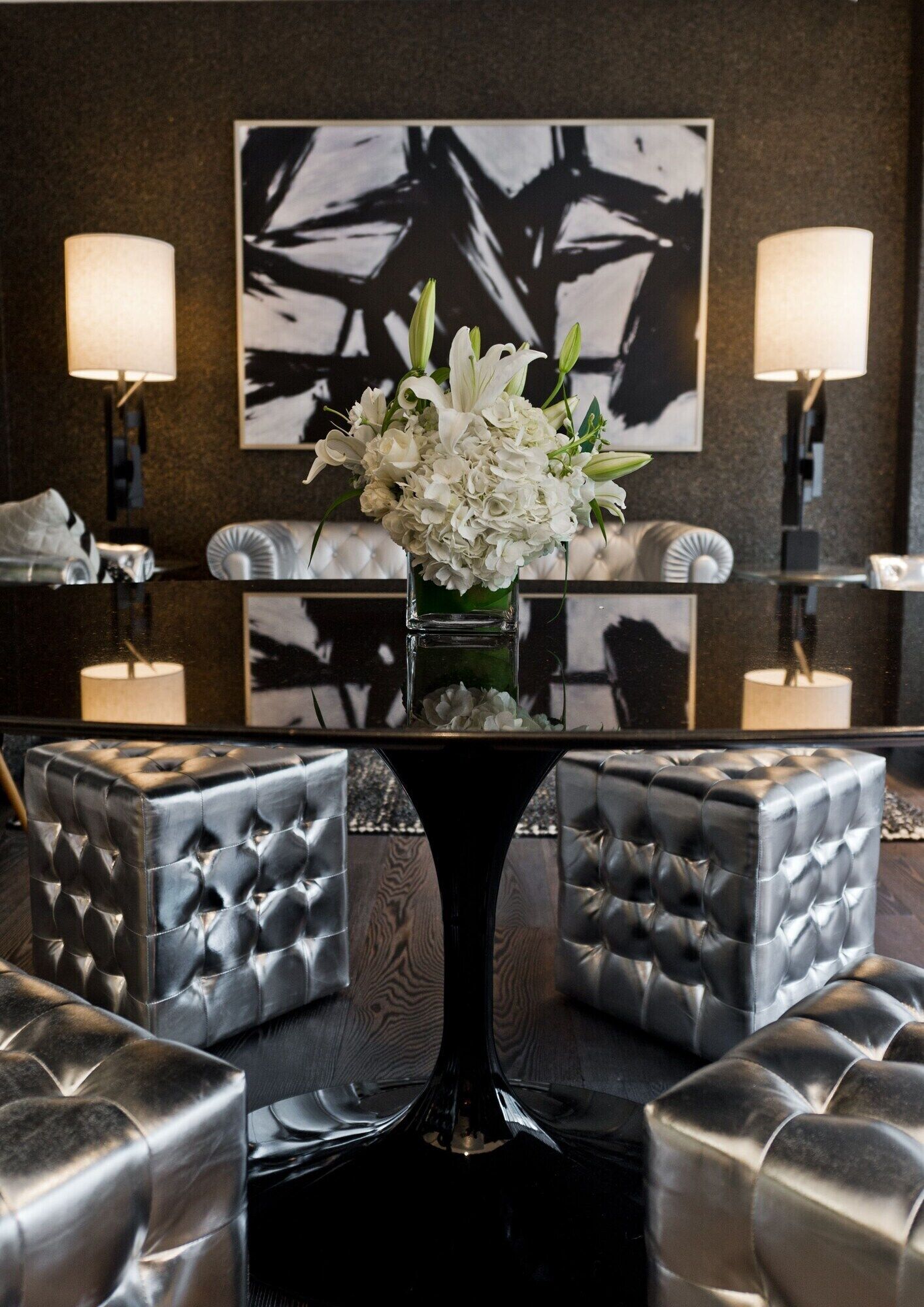 A lobby with a tufted leather sofa, a glass table with a vase of flowers, and a modern abstract painting on the wall.