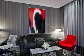 A modern hotel room with a dark grey sofa, a red armchair, a black and white patterned coffee table, and a large abstract painting on the wall. - Moderne | Junior Suite | Steps to Times Square | Extra Living Space (New York)