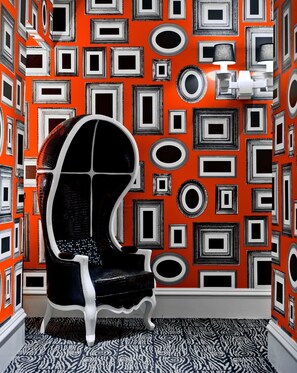Um quarto com uma parede laranja estampada, uma cadeira preta e branca e um tapete padronizado.