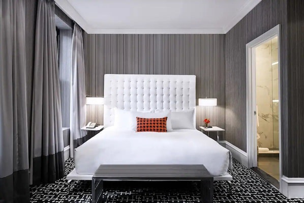 Ein Hotelzimmer mit einem großen Bett, einem Kopfteil, Nachttischen und einer Badezimmertür.