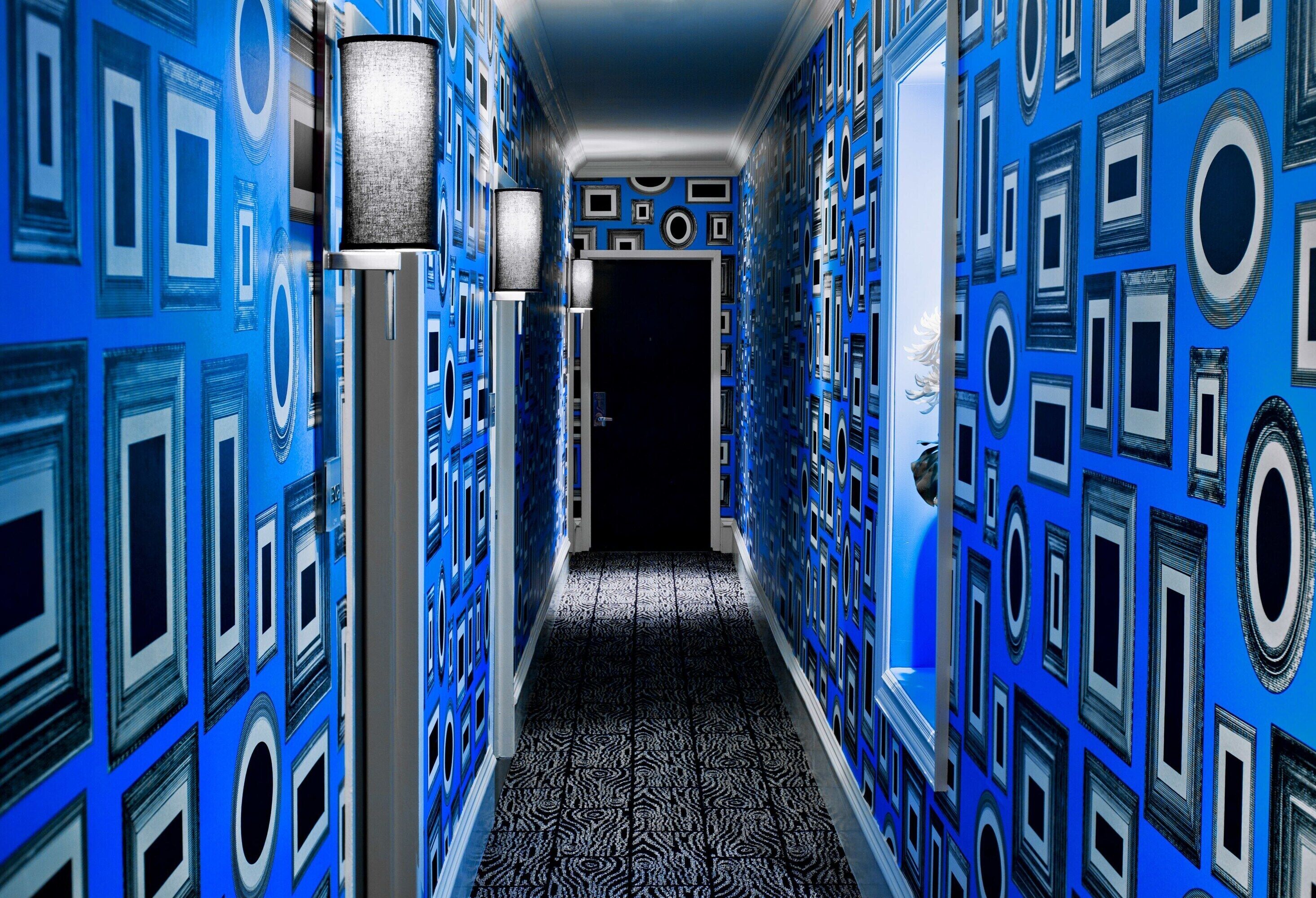 A hallway with patterned walls and a patterned carpet, leading to a dark doorway.
