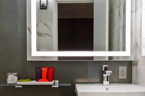 Ein Badezimmer mit einem großen Spiegel, einem weißen Waschbecken und einer Ablage für Toilettenartikel.