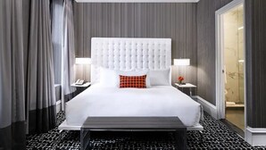 Et hotelværelse med en stor seng, sengebord, sengegavl og en dør til badeværelset.