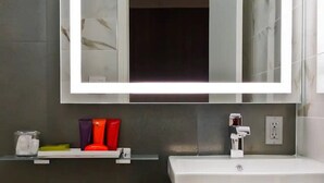 Ein Badezimmer mit einem großen Spiegel, einem weißen Waschbecken und einer Ablage für Toilettenartikel.