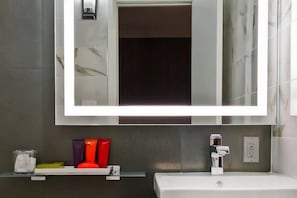 Ein Badezimmer mit einem großen Spiegel, einem weißen Waschbecken und einer Ablage für Toilettenartikel.