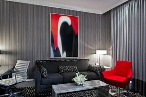A modern hotel room with a dark grey sofa, a red armchair, a black and white patterned coffee table, and a large abstract painting on the wall. - Junior Suite | Moderne | Group NYC Stay | Near Broadway | 2 Units (New York)