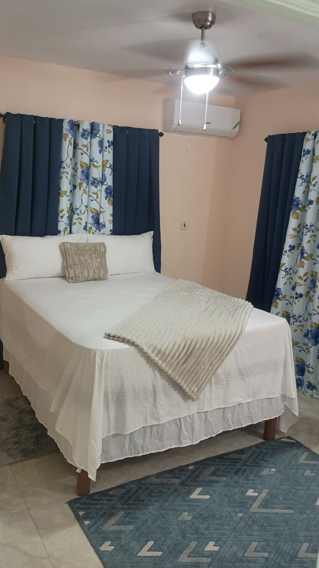 A bedroom with a bed, curtains, a ceiling fan, and a rug.