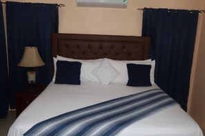 A bed with a brown headboard, white bedding, and two dark blue pillows. - Ocean Breeze Oasis (Montego Bay)