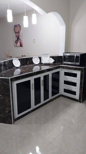 Una cocina con encimera de mármol negro, armarios blancos y un microondas.