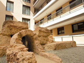 A building with a modern architectural style, featuring a multi-level balcony with railings, large stone structures, and a gravel ground. - Duque 2D · Standard Apartment without Terrace · 2 Bedrooms · 2 Bathrooms (Cordoba)