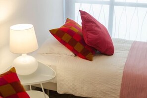 A bed with a white bedspread, a red pillow, and a white lamp on a small white table beside it. - Duque 2D · Standard Apartment without Terrace · 2 Bedrooms · 2 Bathrooms (Cordoba)