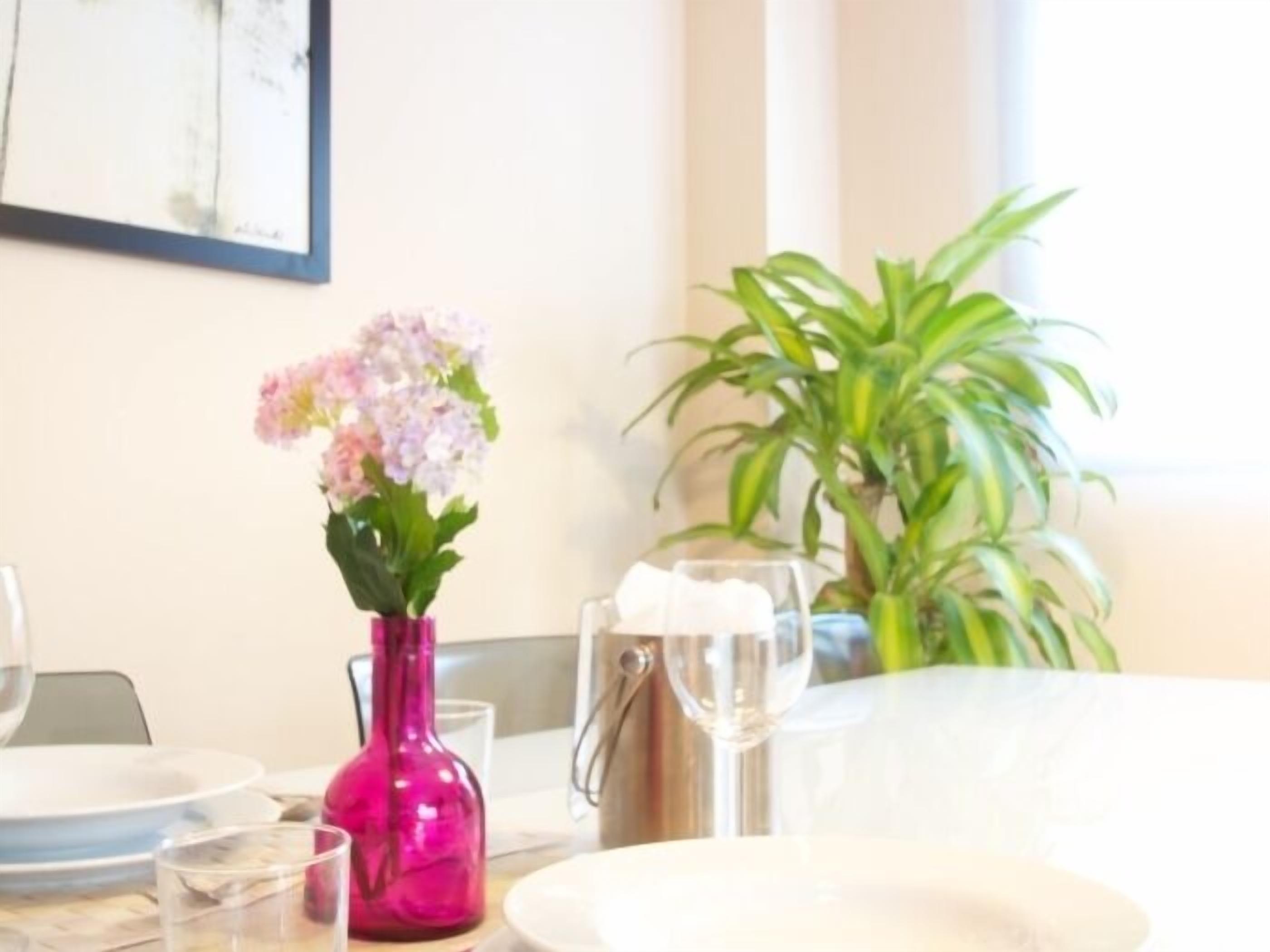 A dining table with a pink vase of flowers, a potted plant, and a wine glass.