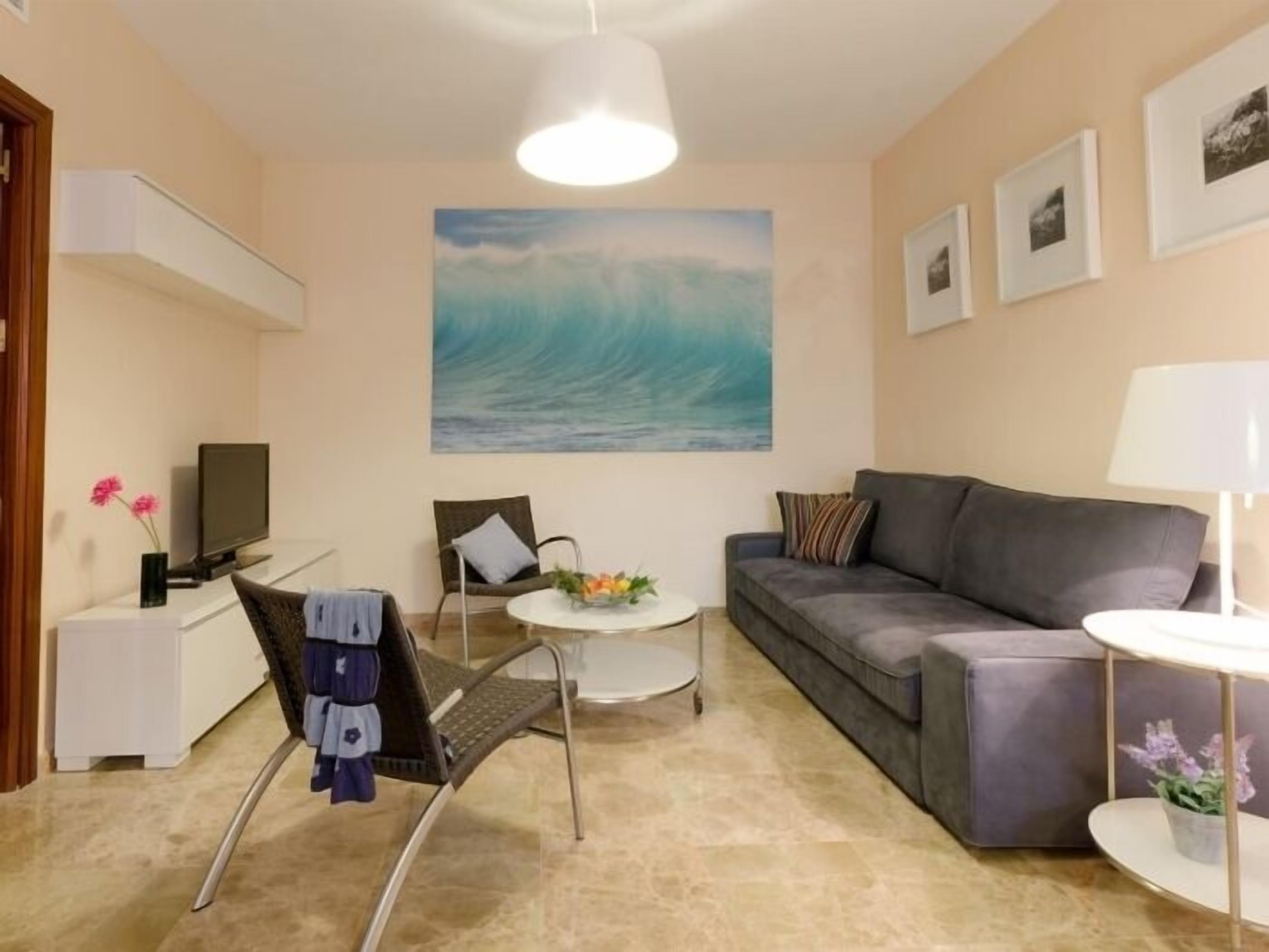 A living room with a sofa, a chair, a small table, a TV, and a painting of a wave on the wall.