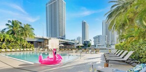 Ein Poolbereich mit Liegestühlen, einem Flamingo-Schwimmding und hohen Gebäuden im Hintergrund.