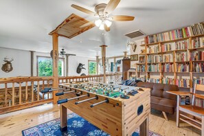 Ein Zimmer mit Tischfußball, Bücherregalen, einem braunen Sofa und einem Deckenventilator.