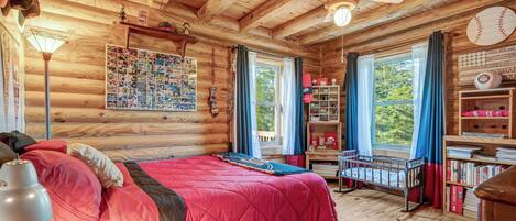 Un dormitorio de cabaña de madera con cama, ventilador de techo, decoración temática de béisbol y una ventana con cortinas.
