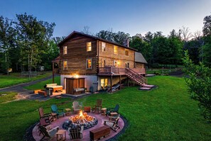 Eine zweigeschossige Holzhütte mit Feuerstelle und Außenbereich mit Sitzgelegenheiten.