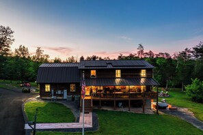 Eine zweistöckige Holzblockhütte mit Veranda, einer überdachten Sitzgelegenheit im Freien und einem gepflegten Rasen.