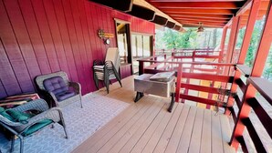 A covered outdoor area with a wooden deck, wicker chairs, a bench, and a metal rack. - Pet-Friendly 3-Bed Retreat near Shasta Lake with cozy wood stove (Lakehead)