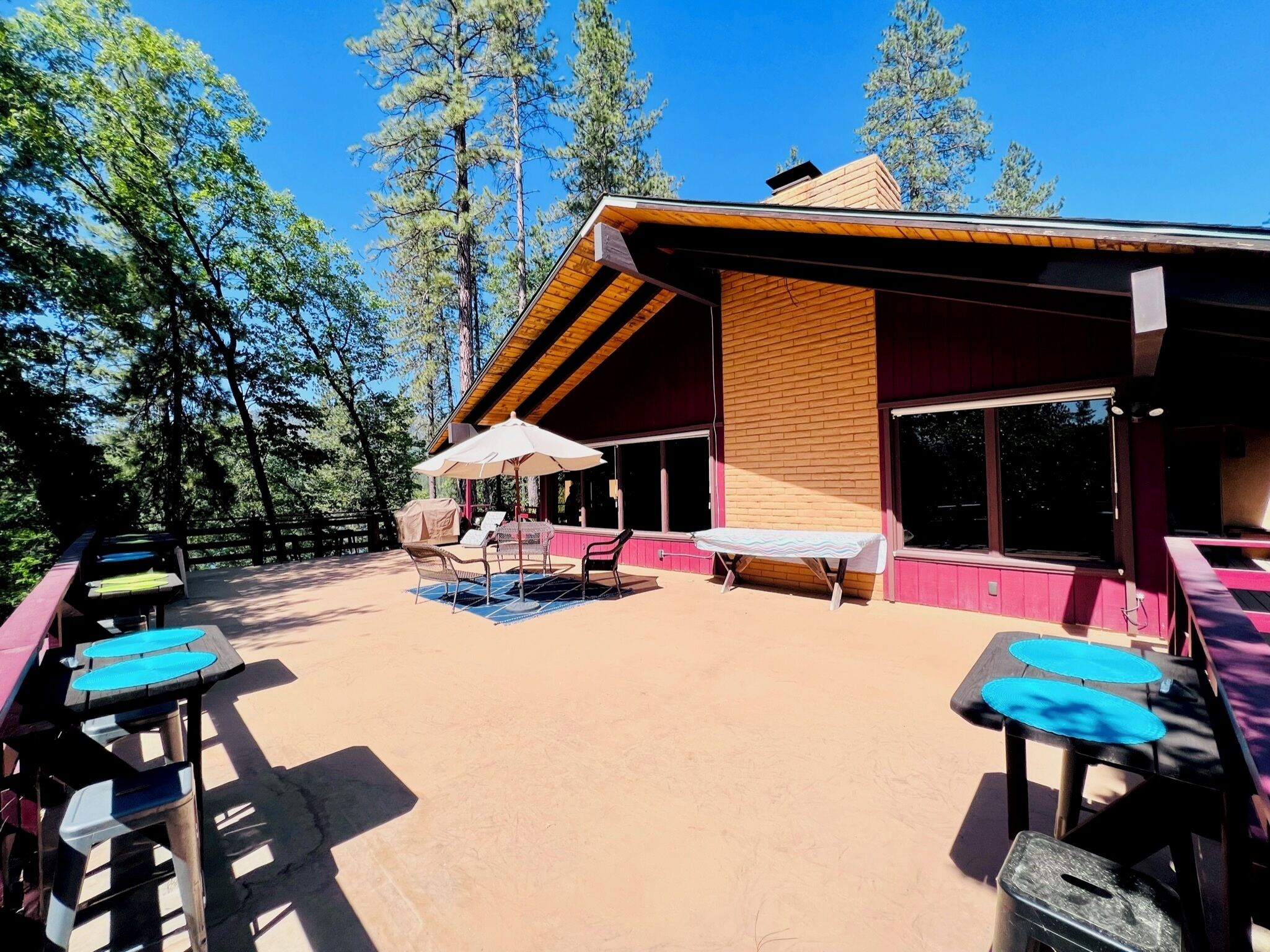 An outdoor patio with tables and chairs, a covered seating area, and a building with large windows and a wooden facade.