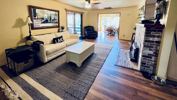 A living room with a sofa, coffee table, patterned rug, fireplace, and a dining area in the background. - Pet-Friendly 3-Bed Retreat near Shasta Lake with cozy wood stove (Lakehead)