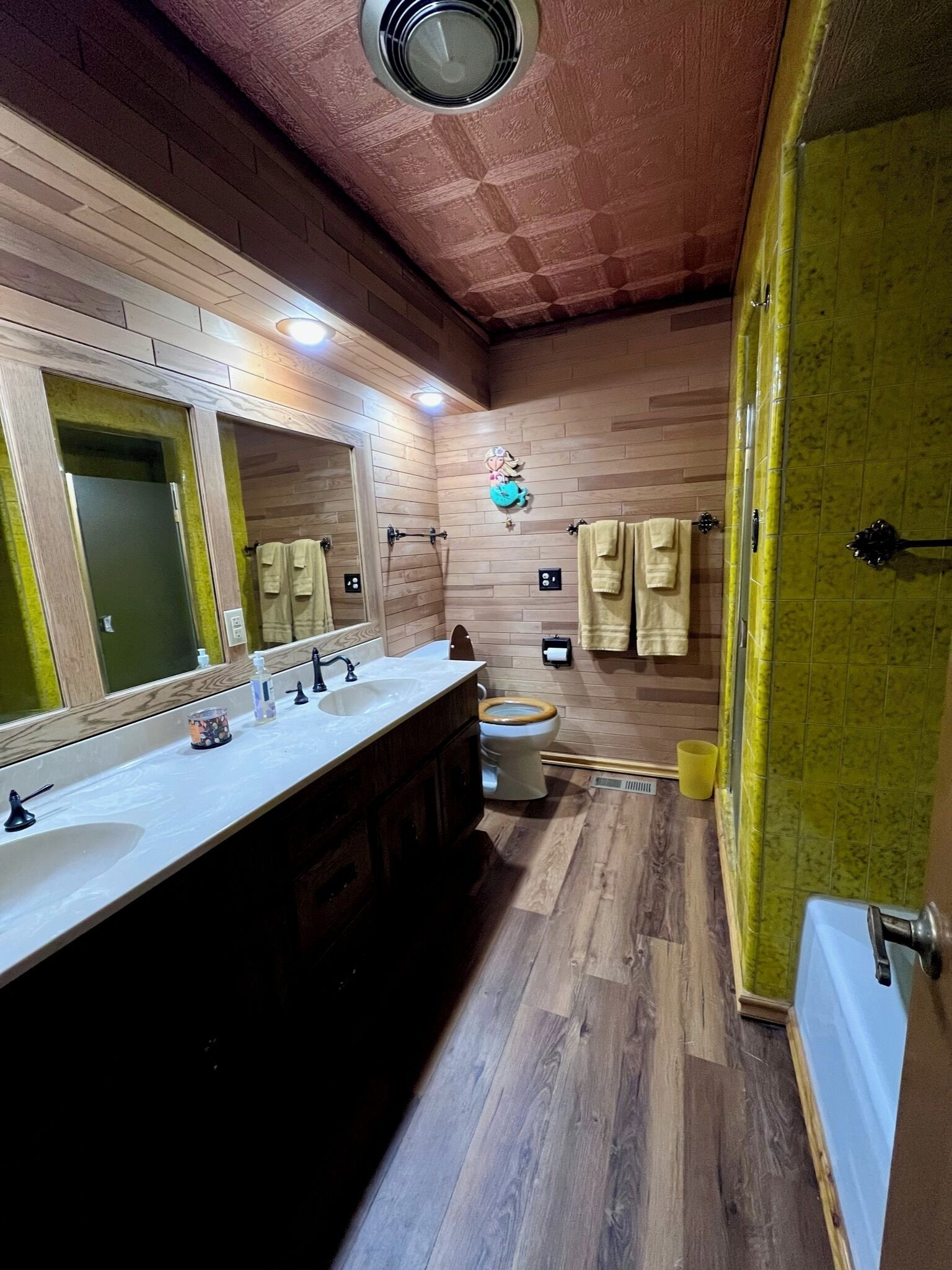 Un baño con suelo de madera, un lavabo con espejo, un inodoro y una zona de ducha.