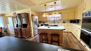 A kitchen with wooden cabinets, a refrigerator, a stove, and a large island with stools. - Pet-Friendly 3-Bed Retreat near Shasta Lake with cozy wood stove (Lakehead)