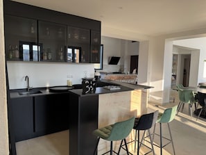 A modern kitchen with a central island, bar stools, and a dining area with chairs. - ⭐ Villa Aetheria: Large Pool, Movie Theater—An Exceptional Villa Near Bordeaux (Ambarès-et-Lagrave)