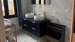 Een moderne badkamer met een donkere wastafel, twee wasbakken, een grote spiegel en een marmeren vloer.