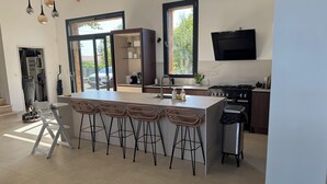 Een moderne keuken met een groot eiland, barkrukken, een ingebouwde oven en een aan de muur bevestigde televisie.
