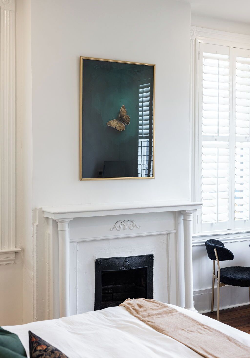 A room with a fireplace, a bed with a blanket, a chair, and a wall-mounted painting.