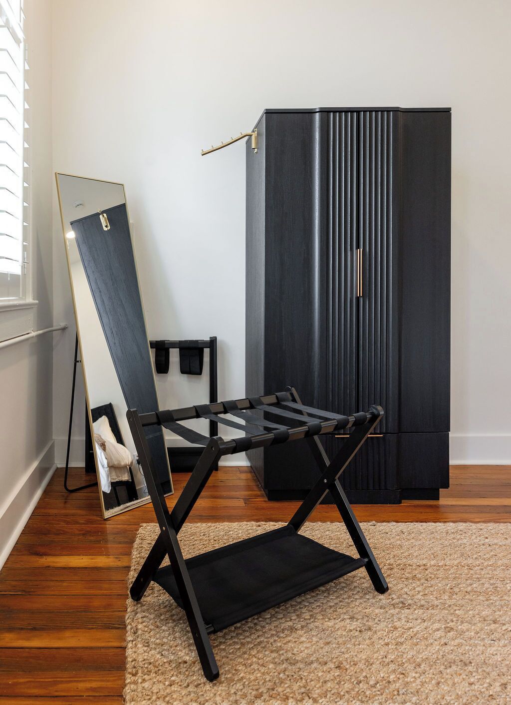 A room with a standing mirror, a black folding chair, a dark-colored wardrobe, and a wooden floor.