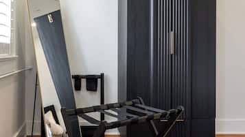 A room with a standing mirror, a black folding chair, a dark-colored wardrobe, and a wooden floor.
