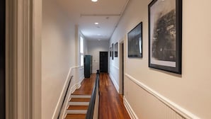 Um corredor com piso de madeira, paredes brancas e quadros na parede direita.