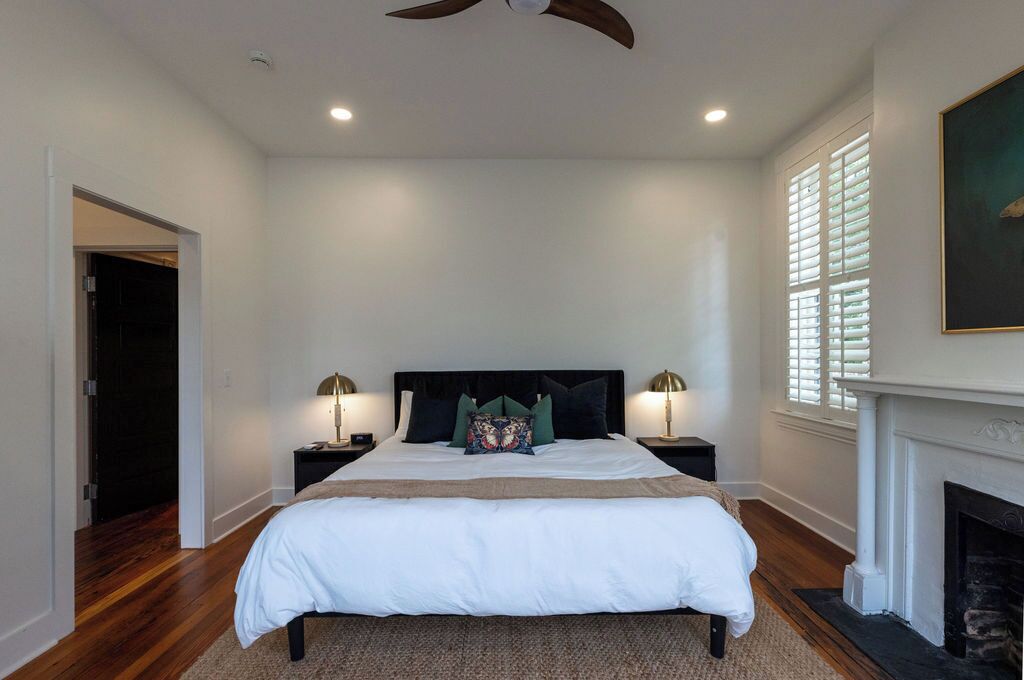 A bedroom with a large bed, two bedside tables with lamps, a fireplace, and a ceiling fan.