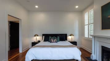 A bedroom with a large bed, two bedside tables with lamps, a fireplace, and a ceiling fan.