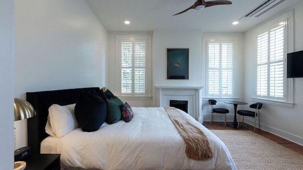 Quarto com cama, ventilador de teto, lareira e televisão na parede.